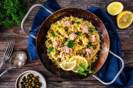 Mediterranean orzo salad with tuna, lemon and capers on wooden background