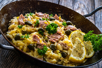 Mediterranean orzo salad with tuna, lemon and capers on wooden background