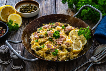 Mediterranean orzo salad with tuna, lemon and capers on wooden background