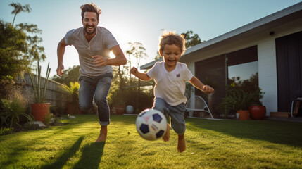 Joyful father and son play with a soccer ball in the front yard of the house - obrazy, fototapety, plakaty