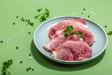 Pieces of pork meat with parsley on gray dish, raw fresh steaks concept. Sea salt, spices