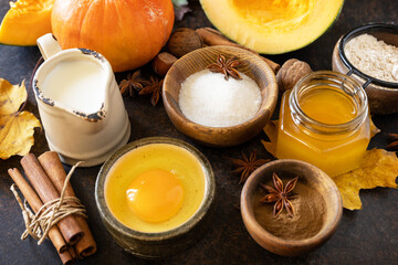 Baking background for Thanksgiving or autumn holidays. Homemade fall baking background with ingredients pumpkins, sugar, flour, nuts, eggs and spices on a dark stone table.