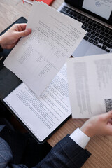 Foreground features a man in a suit holding A4 documents, with an open laptop visible in the background.
