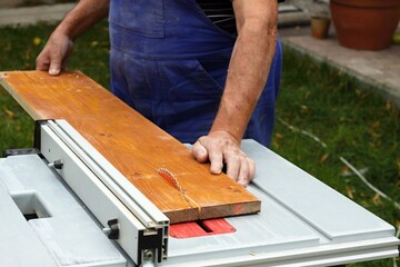 Worker with electric circular saw. Senior carpenter cuts wood, focus on saw,  previously injured fingers can be seen.