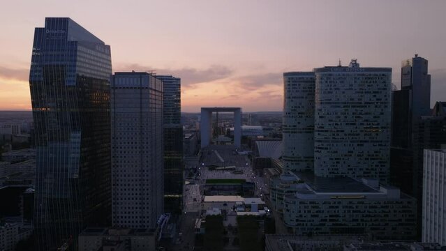 Backwards fly between rows of skyscrapers in futuristic La Defense business district at dusk. Paris, France