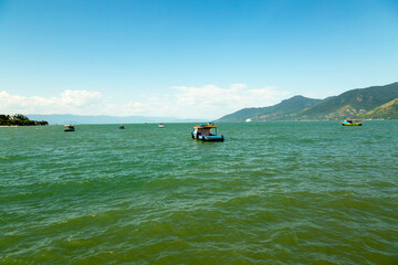 Barcos navegando em mar calmo, céu azul, dia de sol e montanhas ao fundo. São Sebastião, Litoral...