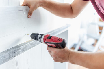 Carpenter installing kitchen chest of drawers by using electrical drill. Home renovation concept.