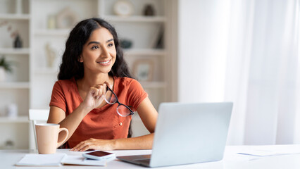 Beautiful young indian woman sitting at desk, working on laptop
