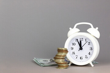 White alarmclock with Coins stack and stack of one hundred dollar bills on grey background. Interest rate and dividend concept, Income, return, retirement, compensation fund, investment dividend tax.