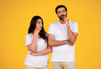 Pensive couple in thought, standing against a yellow background