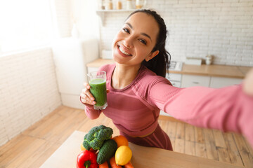 Healthy lady making selfie with green smoothie after workout indoor