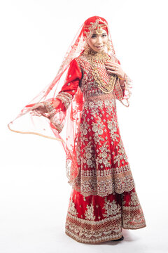 Full height portrait of a beautiful Asian Muslim lady in a hijab wearing a gorgeous Bollywood or Indian themed red traditional wedding dress isolated on white background