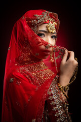 Close up portrait of a beautiful Asian Muslim lady in a hijab wearing a gorgeous Bollywood or Indian themed red traditional wedding dress isolated on dark background