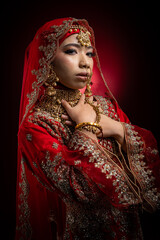 Close up portrait of a beautiful Asian Muslim lady in a hijab wearing a gorgeous Bollywood or Indian themed red traditional wedding dress isolated on dark background
