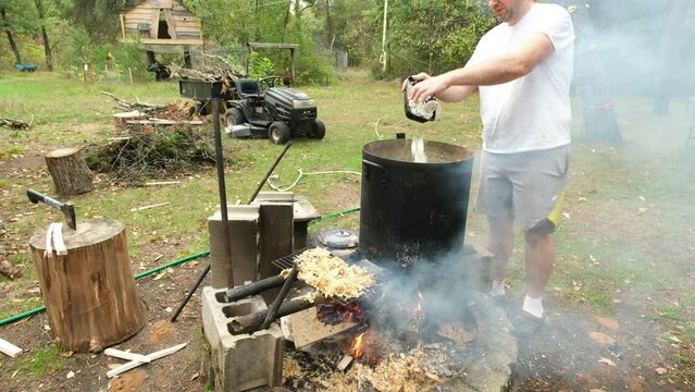 Adding crumbled egg shells for calcium into large pot of steaming liquid while preparing food for animals over fire pit.