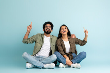 Loving young indian couple pointing at copy space, colored background