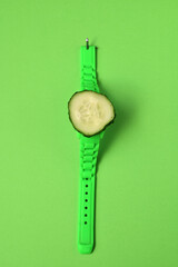 slice of cucumber on a clock on a green background, vegetable season concept