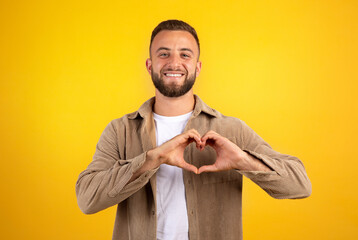Cheerful millennial caucasian guy with beard in casual make heart sign with hands