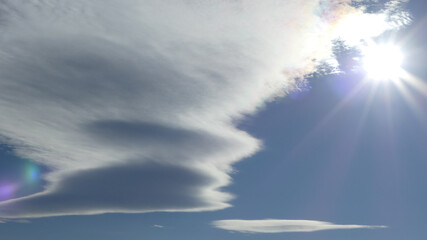 Fototapeta na wymiar Blue sky, sunrays, pearl colors at edge of cloud around sun and Lenticular clouds. Topics: weather, meteorology, climate, sun energy