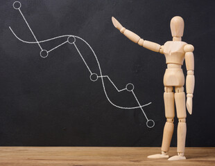 Wooden mannequin points at black chalk board with chart, growth indicators