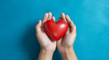 Fototapeta premium Hands holding a red heart on a blue background, heart donation promotion concept