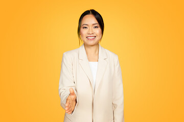 Millennial Asian woman in yellow, extending hand warmly for a handshake, welcoming gesture