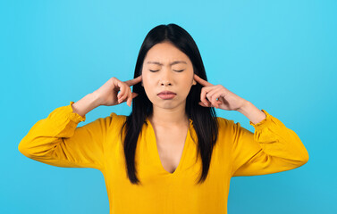 Asian woman wear casual shirt cover ears with hands fingers