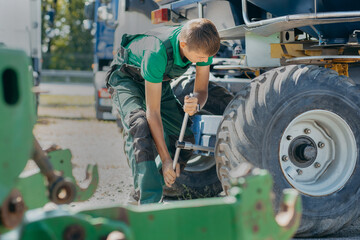 Young mechanic repair tractor outdoor - obrazy, fototapety, plakaty