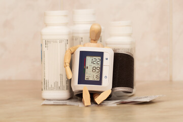 A wooden mannequin sitting with a blood pressure monitor surrounded by cans of pills.