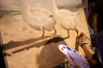 Close-up female artist holds paintbrush and palette with oil paints, working on painting, drawing on canvas in workshop