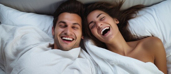 Fototapeta na wymiar Top view of young loving couple lying in bed laughing and smiling with blanket.