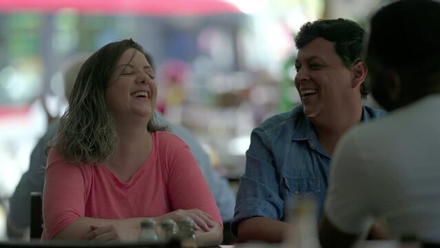 Joyful couple laughing and smiling in candid scene of group of friends at restaurant diner interaction