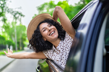 Young girl traveling by car, hispanic woman with curly hair looking out the window, enjoying...