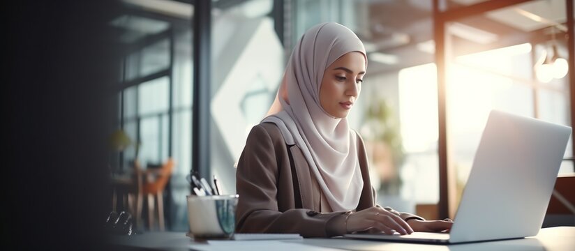 Young businesswoman in hijab sitting at desk in office working online with laptop. Muslim woman working in the office.