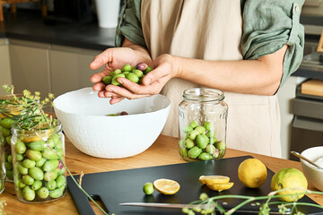 Woman preparing fermented olives in glass jar with slices of lemon, wild fennel and canning brine. Autumn vegetables canning. Healthy homemade food. Conservation of harvest.