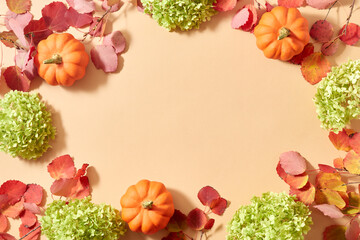 Flat lay frame with colorful autumn leaves and pumpkins on an orange background