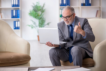 Old male employee sitting on arm-chair