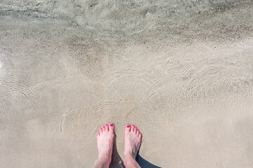 Detail of female feet with pink nail polish on a beautiful beach with pink sand and crystal clear water. Longing for the sea, freedom and summer. Shot in the beautiful pink beach of Elafonissi. - obrazy, fototapety, plakaty