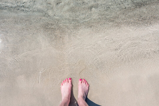 Detail of female feet with pink nail polish on a beautiful beach with pink sand and crystal clear water. Longing for the sea, freedom and summer. Shot in the beautiful pink beach of Elafonissi.
