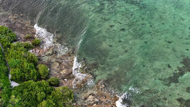 Drone eagle view of coastline with rocky beach and blue Caribbean Sea with waves on a sunny afternoon in Tulum 
