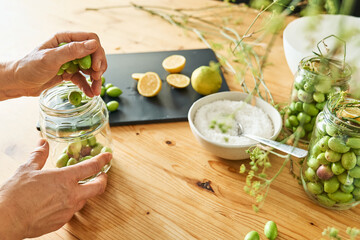 Woman preparing fermented olives in glass jar with slices of lemon, wild fennel and canning brine. Autumn vegetables canning. Healthy homemade food. Conservation of harvest.