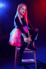 Portrait of a little girl in a clown costume on a dark background in the light of multi-colored spotlights