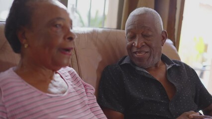 Older couple conversing on couch, a senior black husband and wife talking at home, elderly wife smiling. Relationship at old age - Powered by Adobe