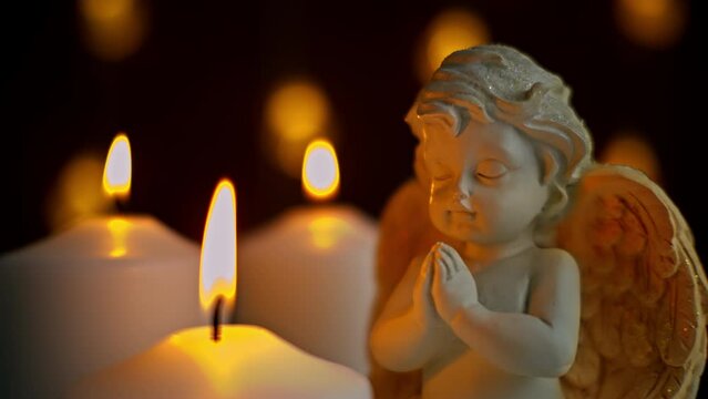 Movement of candle flames with a statuette of a bright angel. Merry Christmas. A holiday in religion. A request in prayer.