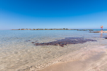 Blonde girl photographs the incredible panorama of Elafonissi pink beach. Gorgeous day and crystal clear water. 