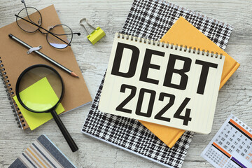 DEBT 2024 text on a notebook with a spiral in the middle of the table near glasses and a magnifying...