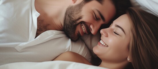 young loving couple lying in bed laughing and smiling with blanket.