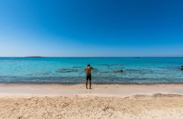 Photo sur Plexiglas  Plage d'Elafonissi, Crète, Grèce Black boy by the sea. Spectacular panorama of Elafonissi Beach in Crete with Turquoise Water and the famous pink sand. The man is wearing a swimsuit and is sunny-side up.