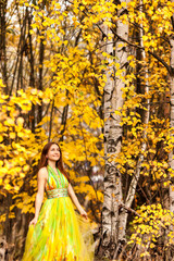 Happy lovely young lady in yellow colored dress posing in autumn park, smile looks up away. Perfect woman model walk in natural fall forest of nature. Golden autumn season concept. Copy ad text space