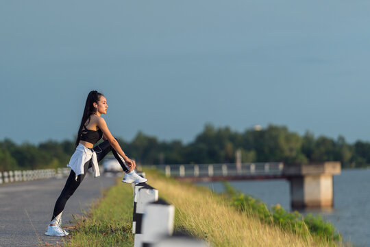 Female jogger standing by a lake tying her shoelaces, Thailand